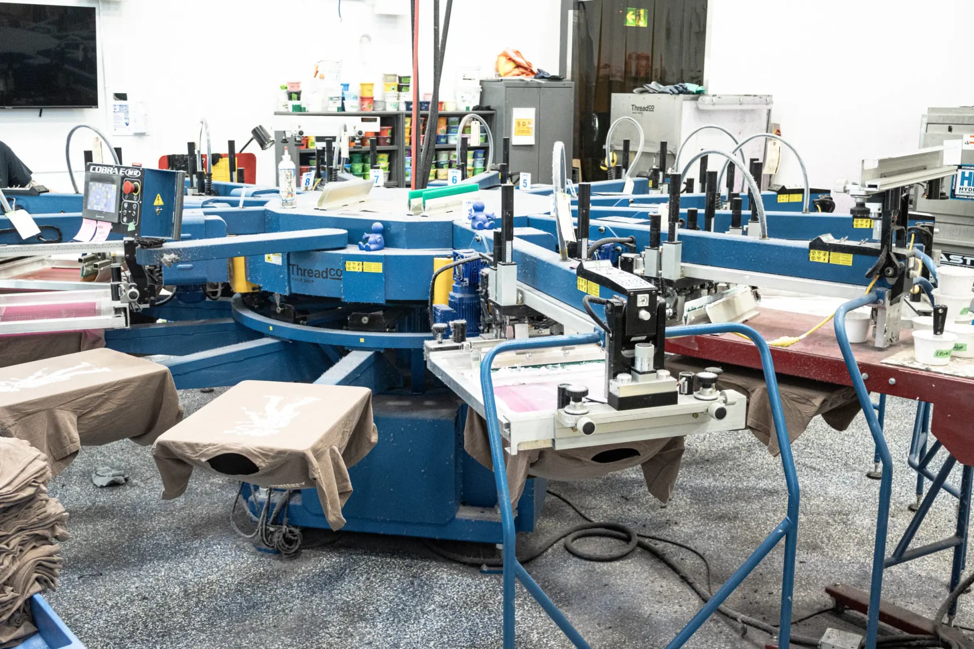 Automatic screen-printing press at ThreadCo Print Shop with freshly printed shirts on the pallets